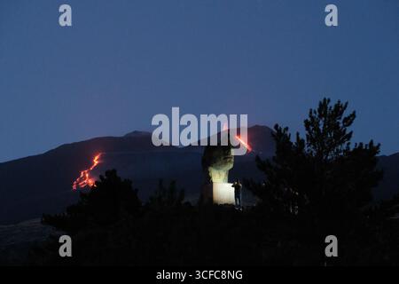 Nell'agosto del 2025 l'Etna entrò in una fase effusiva alimentata da bocche tra bocca nuova e il cratere sudorientale a 2.980–3.200 m s.l.m., inviando freschi corsi di lava lungo la base del cratere sudorientale e sui fianchi sudovest/occidentali superiori. Le immagini mostrano turisti curiosi e gruppi guidati che osservano i flussi luminosi e le esplosioni stromboliane intermittenti al cratere sudorientale, con piccole scogliere di cenere e pennacchi di gas che si disperdono rapidamente. Altri sfiati annotati il 20 e il 21 agosto, con flussi che avanzano da sud a sud-ovest attraverso l'area della cima. Foto Stock
