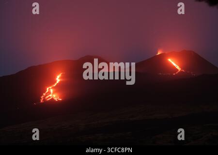 Nell'agosto del 2025 l'Etna entrò in una fase effusiva alimentata da bocche tra bocca nuova e il cratere sudorientale a 2.980–3.200 m s.l.m., inviando freschi corsi di lava lungo la base del cratere sudorientale e sui fianchi sudovest/occidentali superiori. Le immagini mostrano turisti curiosi e gruppi guidati che osservano i flussi luminosi e le esplosioni stromboliane intermittenti al cratere sudorientale, con piccole scogliere di cenere e pennacchi di gas che si disperdono rapidamente. Altri sfiati annotati il 20 e il 21 agosto, con flussi che avanzano da sud a sud-ovest attraverso l'area della cima. Foto Stock