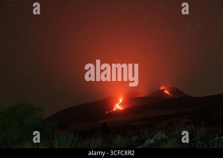 Nell'agosto del 2025 l'Etna entrò in una fase effusiva alimentata da bocche tra bocca nuova e il cratere sudorientale a 2.980–3.200 m s.l.m., inviando freschi corsi di lava lungo la base del cratere sudorientale e sui fianchi sudovest/occidentali superiori. Le immagini mostrano turisti curiosi e gruppi guidati che osservano i flussi luminosi e le esplosioni stromboliane intermittenti al cratere sudorientale, con piccole scogliere di cenere e pennacchi di gas che si disperdono rapidamente. Altri sfiati annotati il 20 e il 21 agosto, con flussi che avanzano da sud a sud-ovest attraverso l'area della cima. Foto Stock