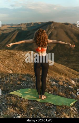 Una donna pratica yoga su un tappetino in cima a una montagna Foto Stock