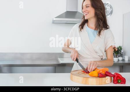 Donna che affetta peperoni rossi e gialli su un tagliere in legno al banco della cucina, spazio copia Foto Stock