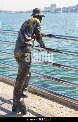 Baku, Azerbaigian - 10 maggio 2025: Statua di bronzo dei pescatori sul viale Baku, affacciata sul Mar Caspio. Skyline della città sullo sfondo. Foto Stock