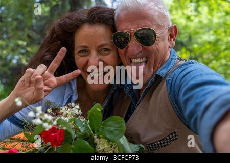 bella e armoniosa coppia di mezza età sorridente e scattata divertenti selfie, facendo segno di pace con la mano all'aperto Foto Stock