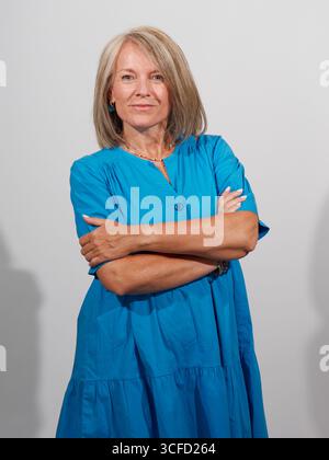 Una donna matura e sicura di sé con un abito blu brillante con le braccia incrociate su uno sfondo semplice. Italia Foto Stock
