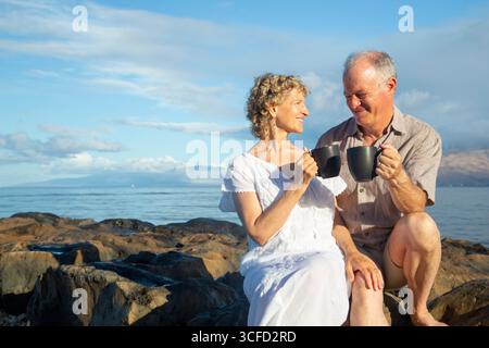Una coppia più anziana si gusta un caffè sulla costa rocciosa in una giornata di sole. Parco Kepaniwai, Wailuku, Hawaii Foto Stock