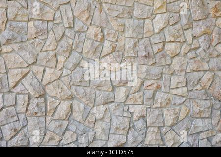 Dettaglio di una parete con un motivo decorativo di pietre grigie irregolari unite con cemento grigio. Vista frontale. Foto Stock