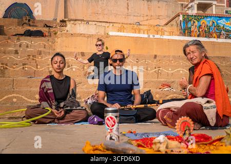 Gruppo variegato di locali e turisti che meditano e adorano i Ghati del fiume Gange a Varanasi, India. Foto Stock