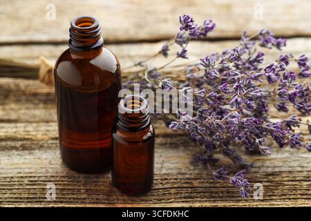 Olio essenziale di lavanda in bottiglie con fiori su tavola di legno, primo piano Foto Stock
