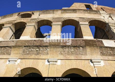 Vista ripida verso l'alto fino alla facciata parzialmente restaurata facciata esterna con grandi finestre ad arco archi archi in mattoni dell'antico Colosseo Romano dall'antichità, RO Foto Stock
