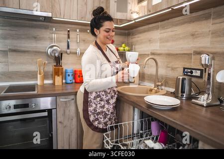 Giovane donna che porta fuori i piatti dalla lavastoviglie Foto Stock