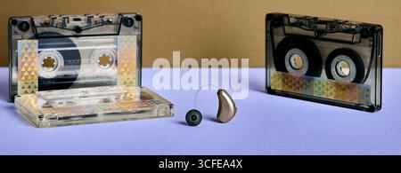 Concetto di udito. L'apparecchio acustico si trova tra due cassette, unendo la tecnologia audio al suono nostalgico Foto Stock