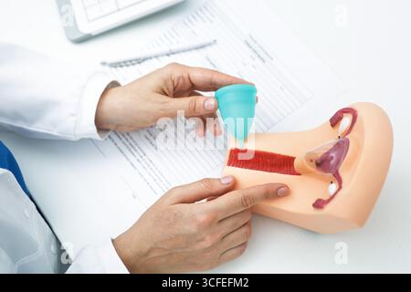 Soluzioni per l'igiene femminile, prodotti d'epoca. Ginecologo che consulta paziente con modello di utero e coppetta mestruale da utilizzare durante le mestruazioni Foto Stock