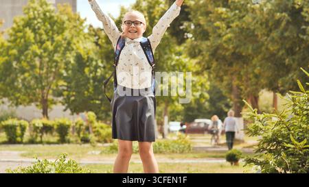 Una studentessa eccitata che salta con le braccia alzate per festeggiare dopo la scuola, godendosi la libertà e la felicità in un parco Foto Stock