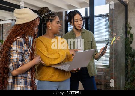 Diverse collaboratrici di sesso femminile che collaborano con notebook e tablet argentati in ufficio con appunti adesivi Foto Stock