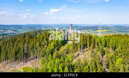 La vista aerea cattura l'impressionante torre di osservazione di Svatobor annidata tra lussureggianti foreste verdi della Cechia, mostrando i dintorni panoramici della torre e il paesaggio lontano. Foto Stock