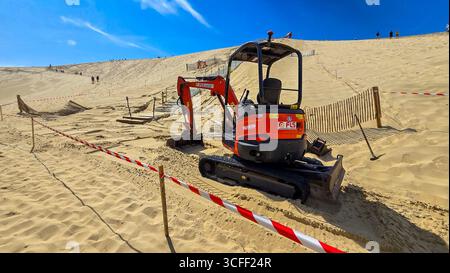 Il processo di costruzione di scale in cemento sulla più grande Dune du Pilat europea dell'Atlantico. In primo piano c'è un escavatore rosso. 12 giugno 2025. La Foto Stock
