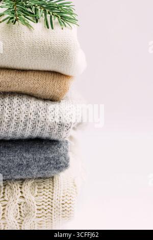 Una pila di comodi pullover in maglia dai colori neutri, con un ramo di pino verde, su sfondo chiaro Foto Stock