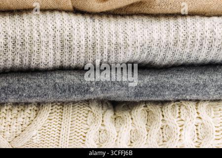 Una pila di comodi pullover in maglia dai colori neutri, che presentano varie texture e motivi Foto Stock