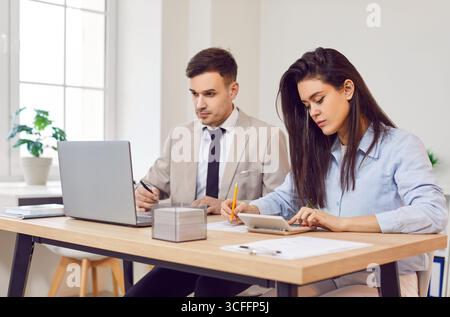 Due commercialisti, uomo e donna, che lavorano in ufficio, calcolano le tasse mensili e analizzano i dati finanziari. Foto Stock