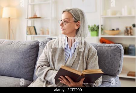 Donna matura e calma che passa il tempo libero a casa da sola, seduta su un comodo divano Foto Stock