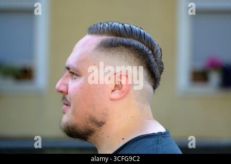 Un giovane uomo con un taglio di capelli ben curato caratterizzato da una superficie rasata sbiadita e pettinata viene catturato all'aperto con un profilo laterale. Foto Stock