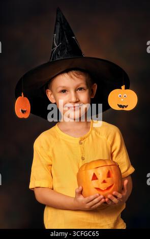 Affascinante ritratto autunnale di un ragazzo sorridente che tiene in mano la zucca scolpita ad Halloween Foto Stock