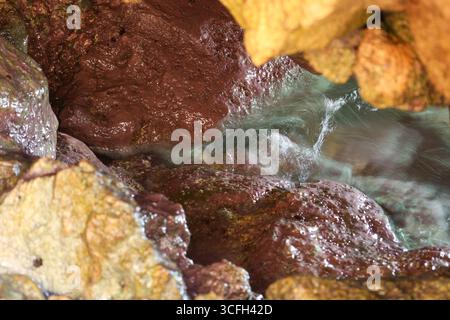Vista ravvicinata di rocce colorate bagnate con acqua di mare che scorre all'interno di una grotta marina. Foto Stock