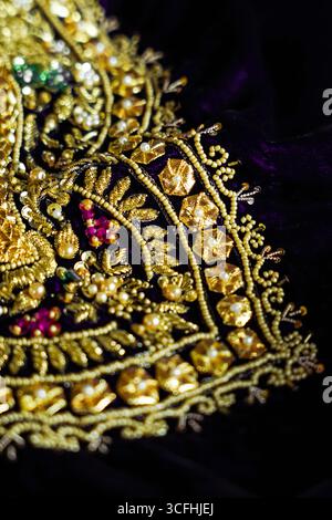 Dettagli ravvicinati di squisiti ricami dorati su un ricco tessuto di velluto viola. Il design intricato presenta perline, paillettes e fili metallici, showca Foto Stock