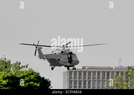 Royal Netherlands Navy NH90 N-326 che vola in basso sopra Amsterdam, Paesi Bassi, elicottero con porta laterale aperta e carrello di atterraggio giù vicino a un edificio di uffici Foto Stock