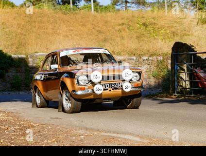 Auto da rally ford di scorta RS d'epoca su una strada soleggiata, classico design marrone bronzo e nero con targhe bianche in un paesaggio paesaggistico di campagna Foto Stock