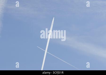 Due aerei passeggeri a reazione con piste di vapore o corrimano che volano in un attraversamento del cielo blu che fa una croce, Inghilterra, Regno Unito Foto Stock
