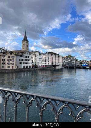 Vista della chiesa di San Pietro di Zurigo con la sua grande torre dell'orologio e gli edifici colorati lungo il fiume Limmat, in Svizzera. Foto Stock