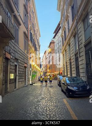 ROMA, ITALIA - 31 LUGLIO 2025 Vista serale lungo una stretta strada acciottolata di Roma, fiancheggiata da alti edifici storici. Atmosfera calda e invitante Foto Stock