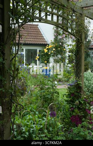 Lush garden brimming with colorful flowers and greenery, seen through a wooden arch at a cozy home during a sunny day. Foto Stock