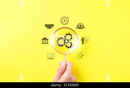 Crescita aziendale e target di marketing. Tenere una lente d'ingrandimento con una ruota dentata come concetto di unità e lavoro di squadra nel luogo di lavoro aziendale. Obiettivo Foto Stock