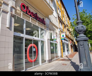 Nagykanizsa, Ungheria - 18 maggio 2025: Moderna filiale di Oberbank con facciata in vetro e segnaletica rossa situata in una strada pedonale con tradizionale Foto Stock