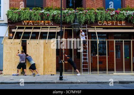 Londra, Regno Unito. 23 agosto 2025. I proprietari d'affari preparano i preparativi finali sabato sera prima del Carnevale di Notting Hill salendo al pub Walmer Castle, che attirerà circa due milioni di persone in questa zona per la festa di strada più grande d'Europa. Credito: Fotografia dell'undicesima ora/Alamy Live News Foto Stock