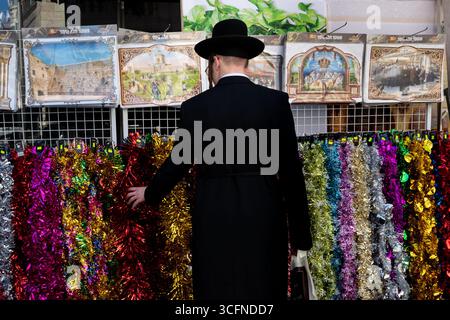 Un uomo ebreo ortodosso esamina stringhe di tinsel colorate usate come decorazione nella Sukkah durante la festa ebraica di Sukkot in Israele. Foto Stock
