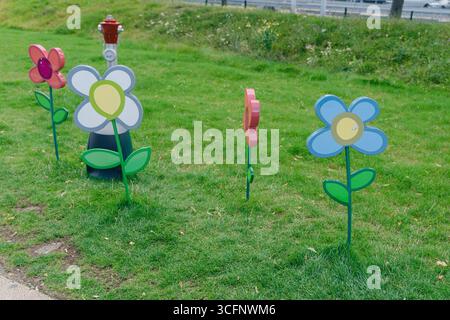 otto fiori di carta colorati sparsi su erba verde. I colori vivaci si sviluppano in blu, rosa, giallo e bianco in contrasto con lo sfondo naturale Foto Stock
