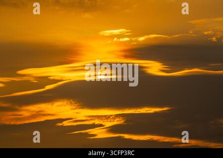 Un incredibile teleobiettivo in primo piano del sole che tramonta, che brilla di calore intenso in un bellissimo cielo arancione Foto Stock