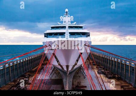 Trasporto di un grande e costoso yacht attraverso l'oceano su una nave pesante. Foto Stock