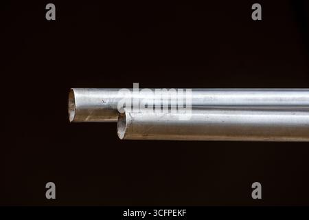 Primo piano di due tubi in acciaio inossidabile usati, con una trama usurata e graffiata su uno sfondo scuro. Stile industriale e grunge con un'attenzione particolare al meta Foto Stock