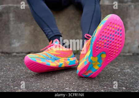 Primo piano di una persona che indossa scarpe da running colorate con suole luminose sedute sul marciapiede. Concetto di fitness, stile di vita attivo e allenamento o all'aperto Foto Stock