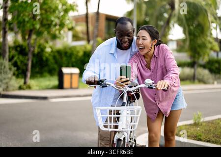 Coppia interrazziale che si diverte a fare un giro in bicicletta, celebrando l'amore, la diversità e l'amicizia Foto Stock