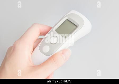 Mano femminile che tiene in mano un moderno termometro a infrarossi isolato su sfondo bianco. Moderno termometro medico durante un'epidemia. Controllo delle malattie infettive Foto Stock