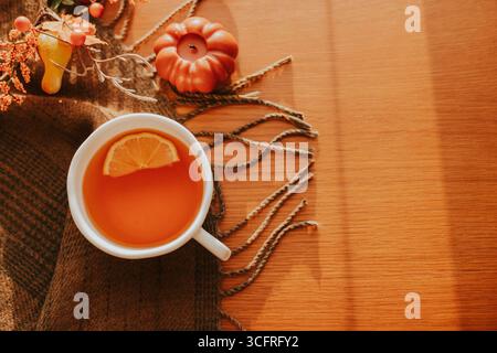 Un tè caldo servito in una tazza bianca con una fetta di limone, circondato da un'accogliente disposizione autunnale con piccole zucche, foglie e texture rustiche Foto Stock