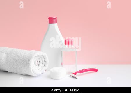 Igiene e cura del corpo. Lozione corpo acqua micellare, asciugamano, rasoio, batuffoli di cotone su sfondo rosa, trattamenti spa e femminili. Concetto di epilazione Foto Stock