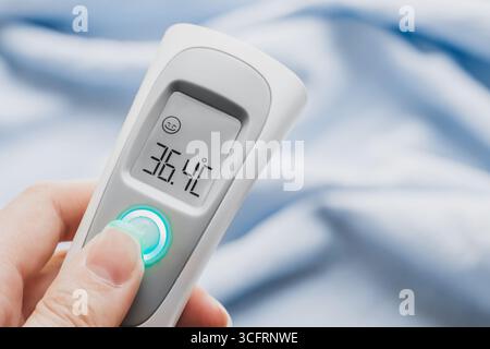 Termometro a infrarossi con presa a mano a temperatura normale. primo piano. Dispositivo di misurazione della temperatura a infrarossi. Azione sanitaria a domicilio. Termometro senza contatto Foto Stock
