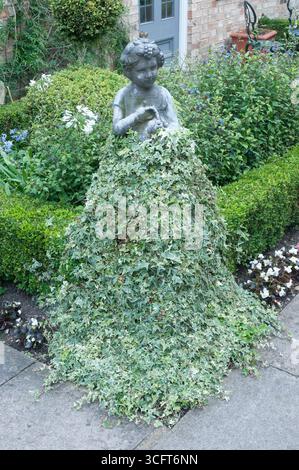 Un incantevole giardino presenta una statua di una ragazza circondata da lussureggiante vegetazione, creando una scena stravagante piena di fiori vibranti. Foto Stock