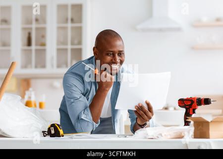 Buon uomo nero che legge le istruzioni di installazione, tenendo il cacciavite nell'interno della cucina Foto Stock